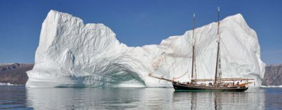 Ein gewaltiger Eisberg türmt sich hinter dem Segelschiff Opal auf